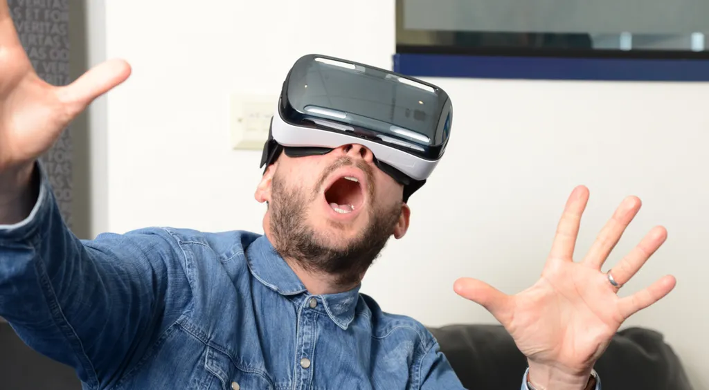 Man wearing a denim jacket with a VR headset on, as he sits on a sofa 
